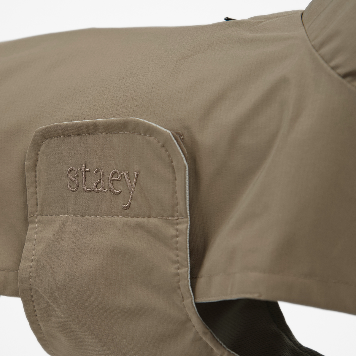 Close-up of the embossed Staey wordmark on the taupe dog rain coat