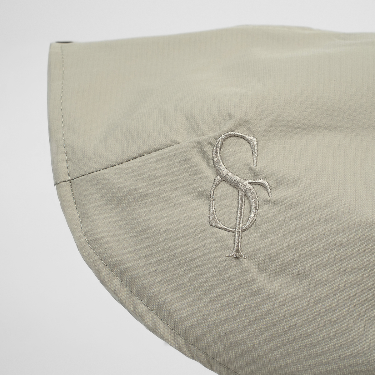 Close-up of the embossed Staey monogram on the nature beige rain coat